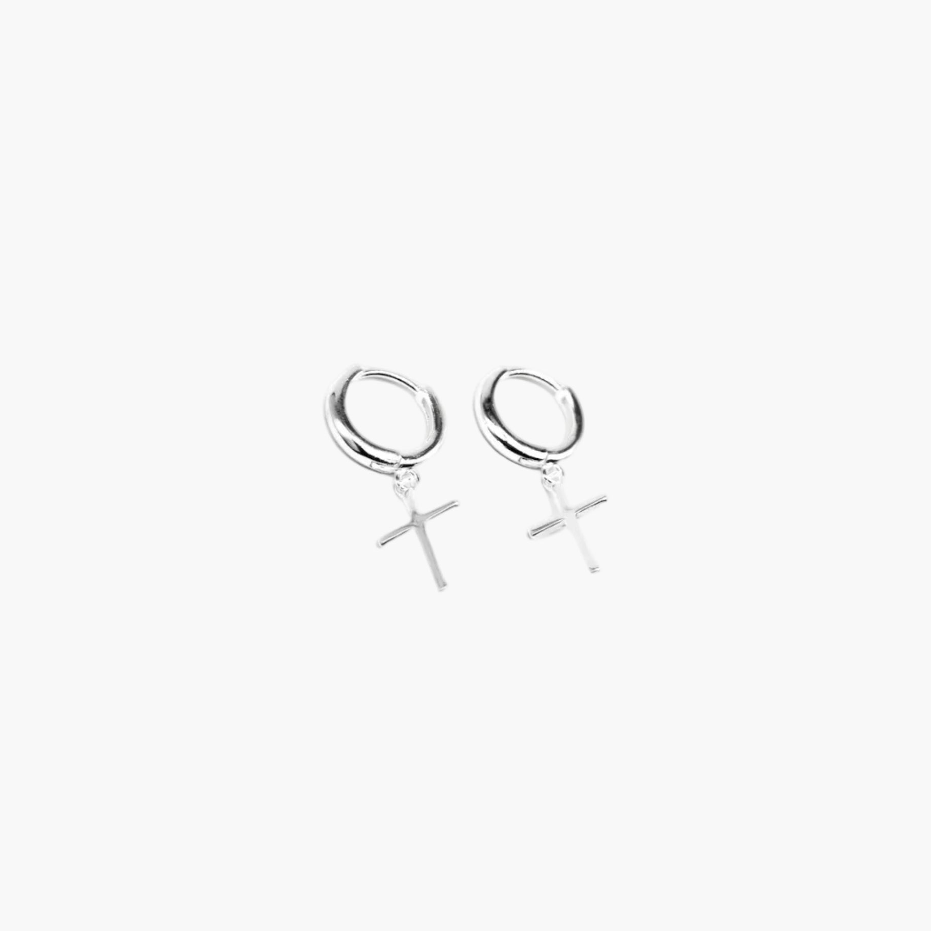 Close-up of silver cross hoop earrings showing precise sculpted cross and smooth finish.